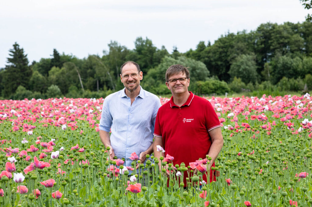 Gerhard Winkler und Mohnbauer Andreas Greßl stehen im Mohnfeld und blicken in die Kamera.